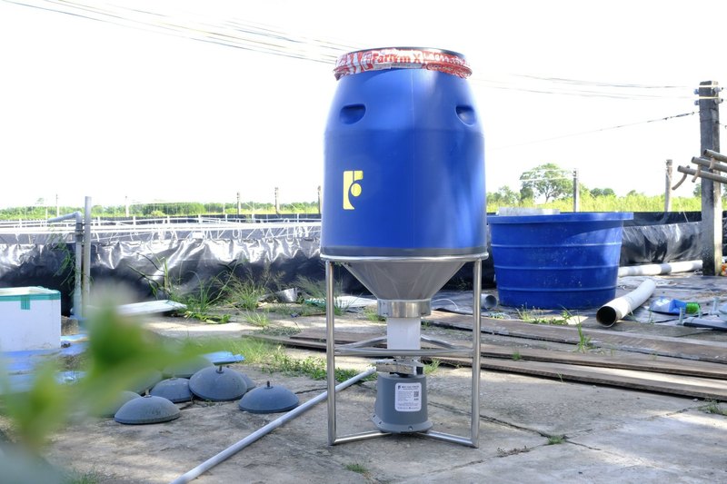 Máy cho tôm ăn FarmX A50 phễu inox thùng xanh lắp xong nhìn thẳng, thấy khung inox bốn chân và hộp mô tơ dưới đáy phễu, xưởng FarmX Đầm Dơi Cà Mau
