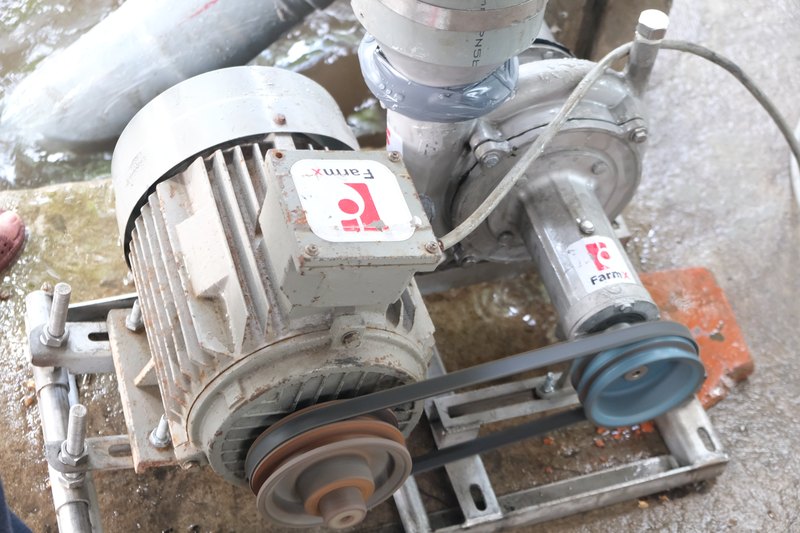 Bơm tuhit FarmX F1 nhìn nghiêng tại khu chạy thử của xưởng, thấy mô tơ, dây cu roa và bầu bơm dán tem FarmX