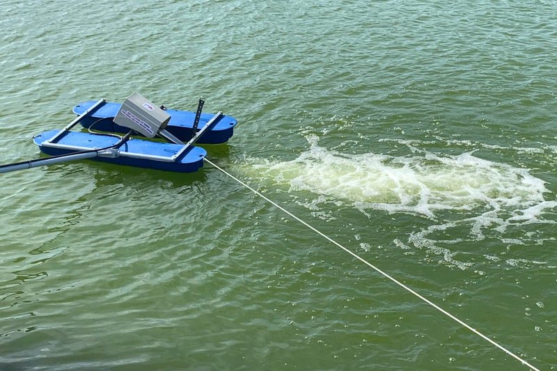 Máy sục khí FarmX OxyJet trên nổi trên mặt nước xanh, dây neo kéo căng, luồng bọt trắng phun dài phía sau, xưởng FarmX Đầm Dơi Cà Mau